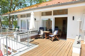 A covered outdoor deck with wooden flooring, two lounge chairs, a small table, and a white umbrella.