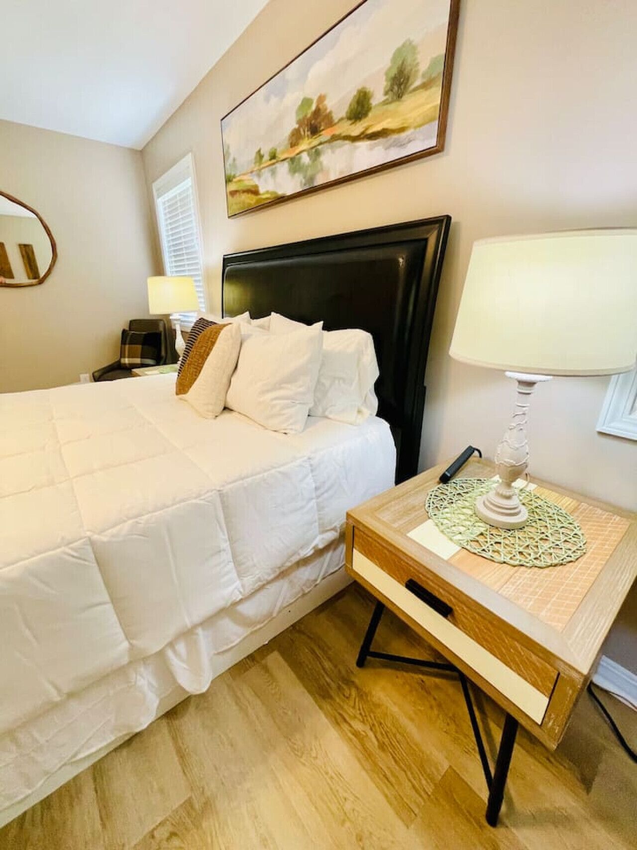 A hotel room with a large bed, a bedside table with a lamp, and a painting on the wall.