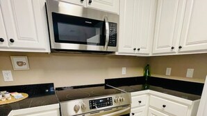 Una cucina con mobili bianchi, un forno a microonde in acciaio inossidabile, un forno e un piano di lavoro nero.