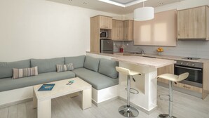 A modern kitchen with a built-in oven, a microwave, and a sink. There is a grey sofa with cushions and a small white table with a magazine. - Superior ενός υπνοδωμάτιού, Erietta Apartments (Zakynthos)