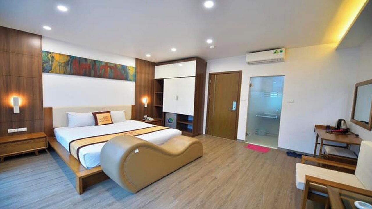 A modern hotel room with a large bed, a desk, a chair, and a wardrobe.
