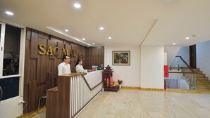 A reception area with a wooden reception desk, a staircase, and a painting on the wall. - Sac Mau Hotel HN - by Bay Luxury (Hanoi)