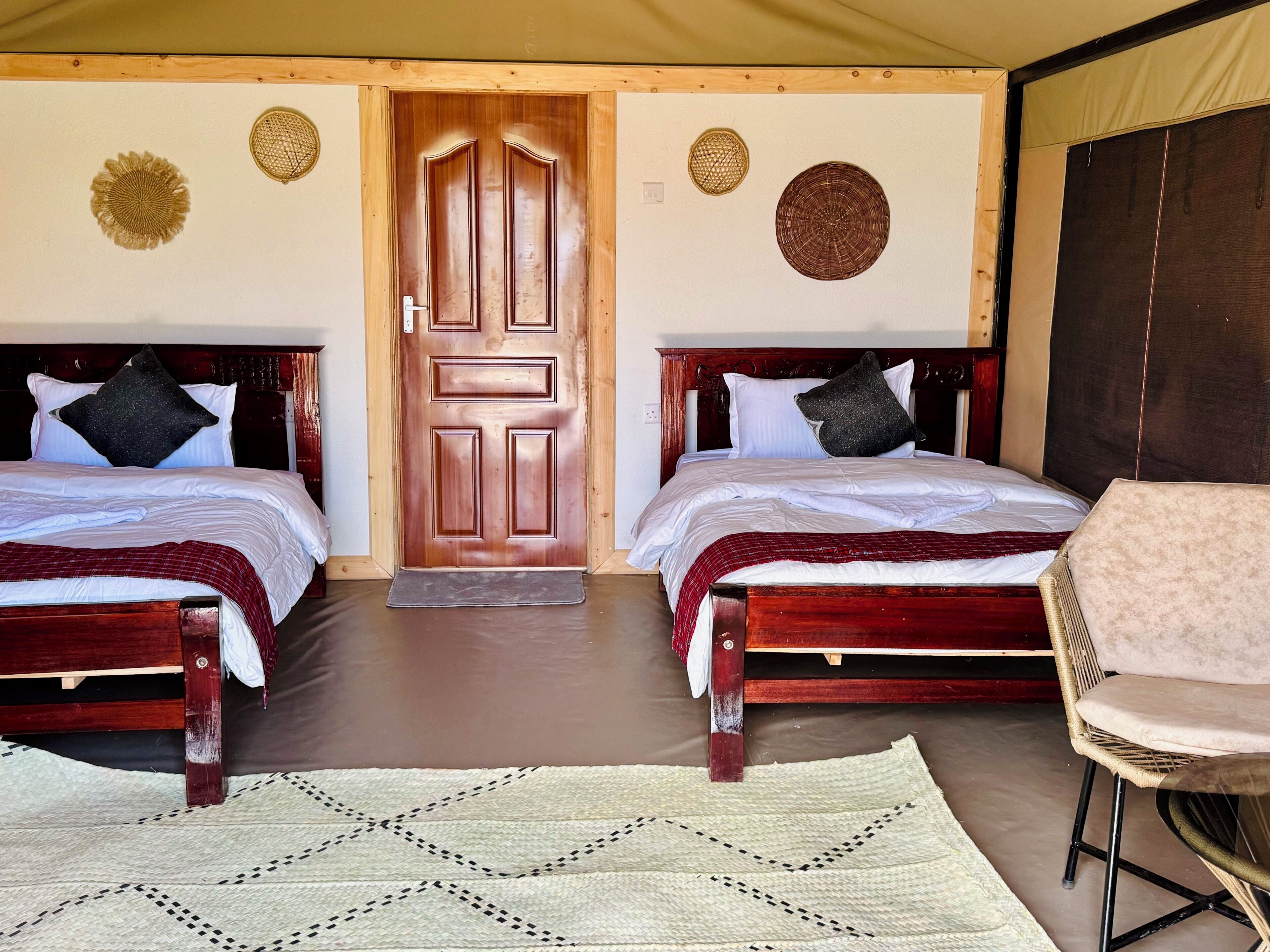 A room with two wooden beds, a chair, a woven rug, and a door with a wooden frame.