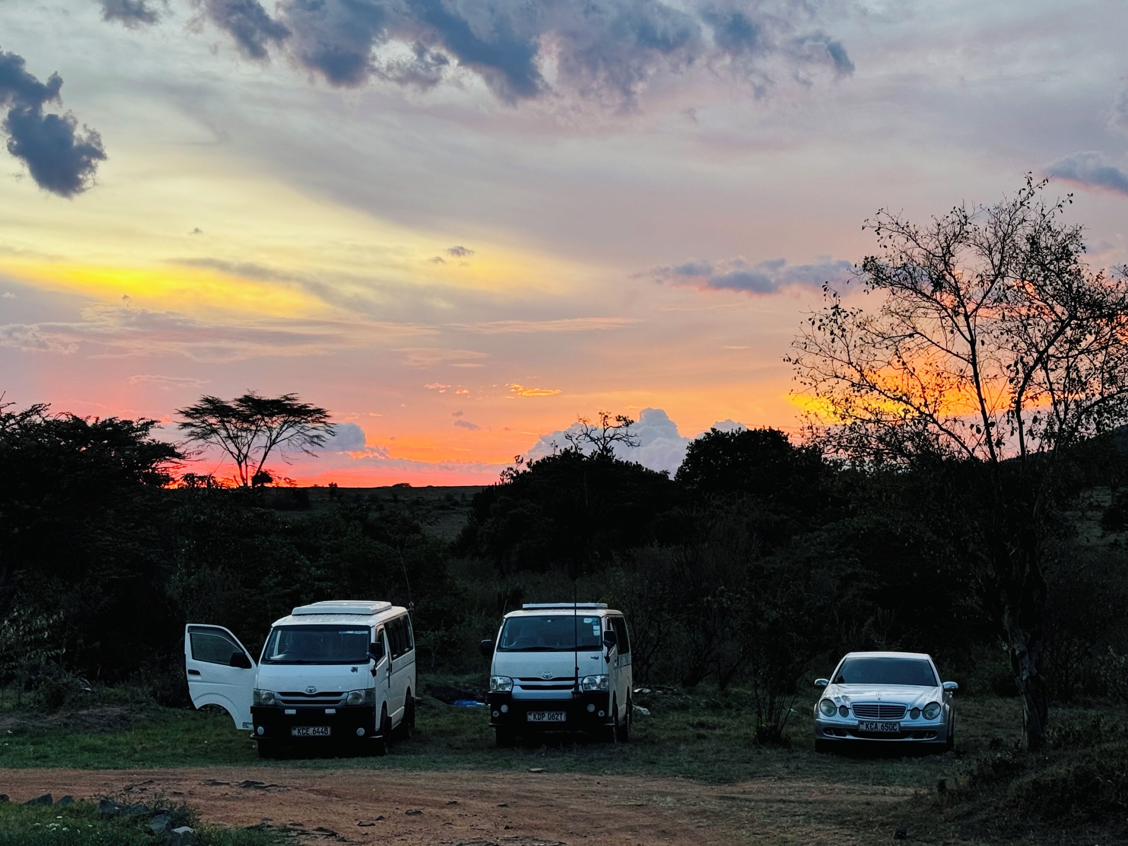Three vehicles parked in a natural setting with a sunset in the background.
