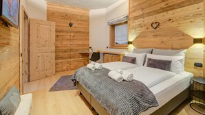 Een slaapkamer met houten lambrisering, een bed, kussens, een bureau en een televisie.