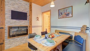 Een eetgedeelte met een houten tafel gedekt voor twee personen, een open haard en een schilderij aan de muur.