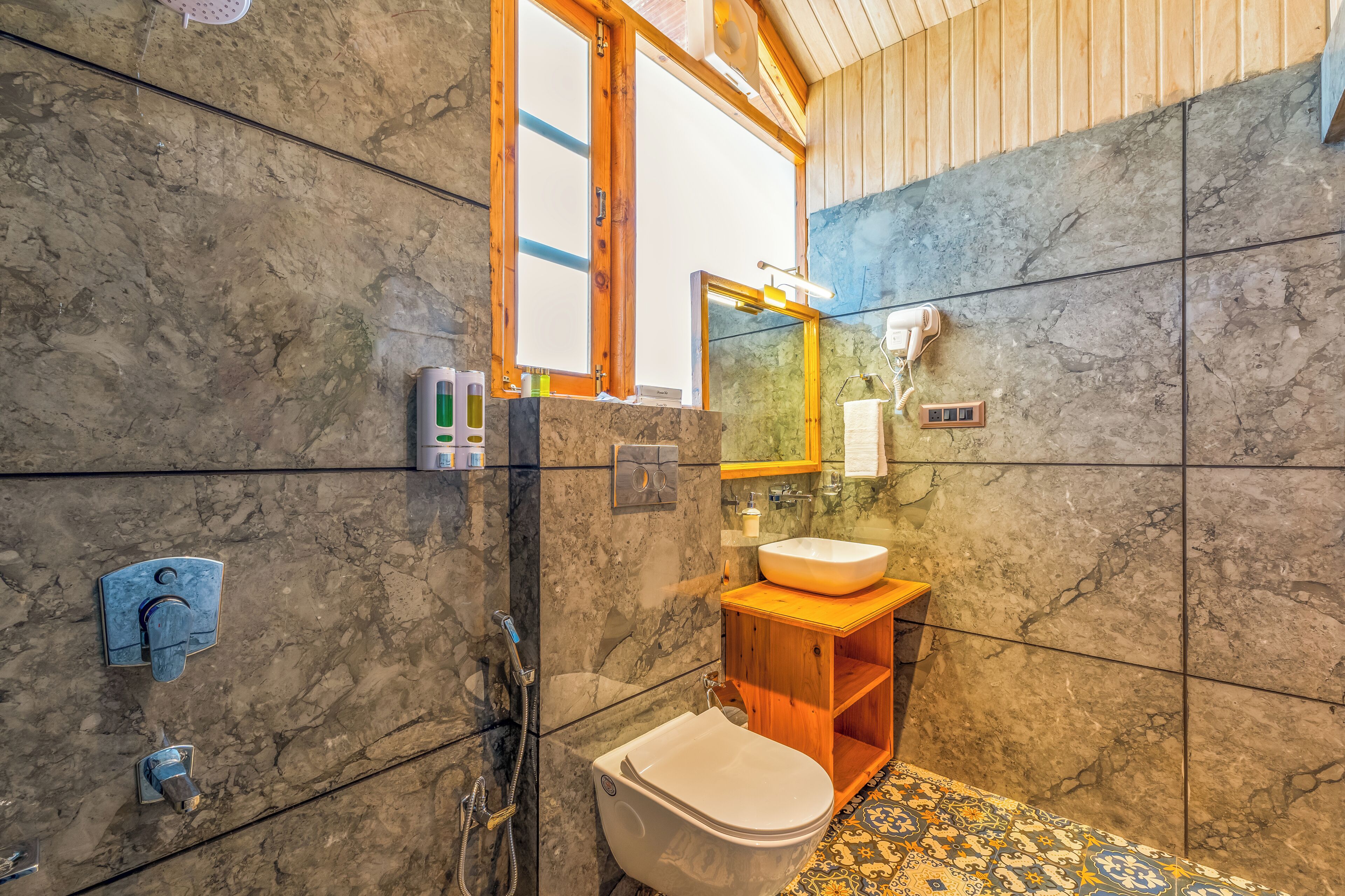 A bathroom with a marble floor, wooden vanity, and a large mirror.