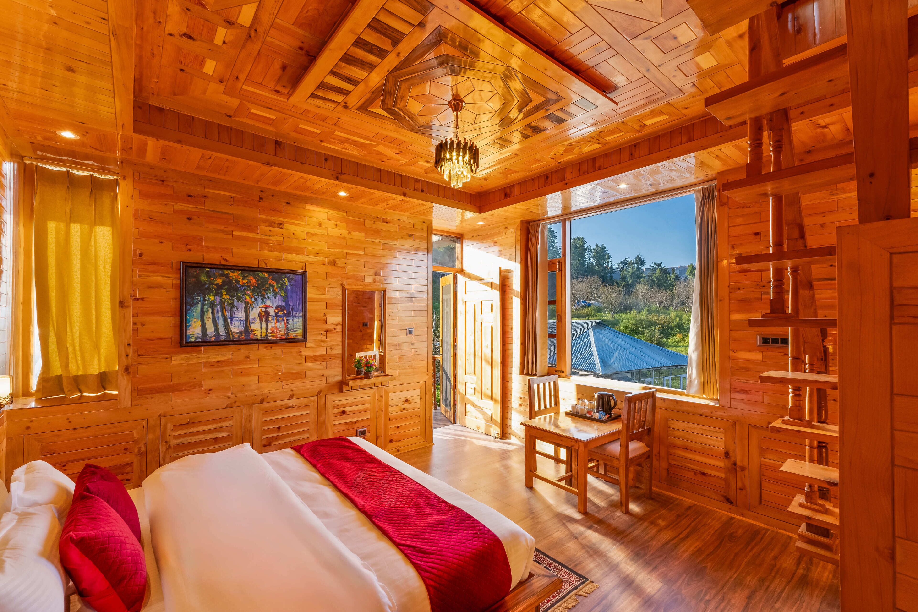 A wooden cabin with a large bed, a dining area, and a view of the outdoors.