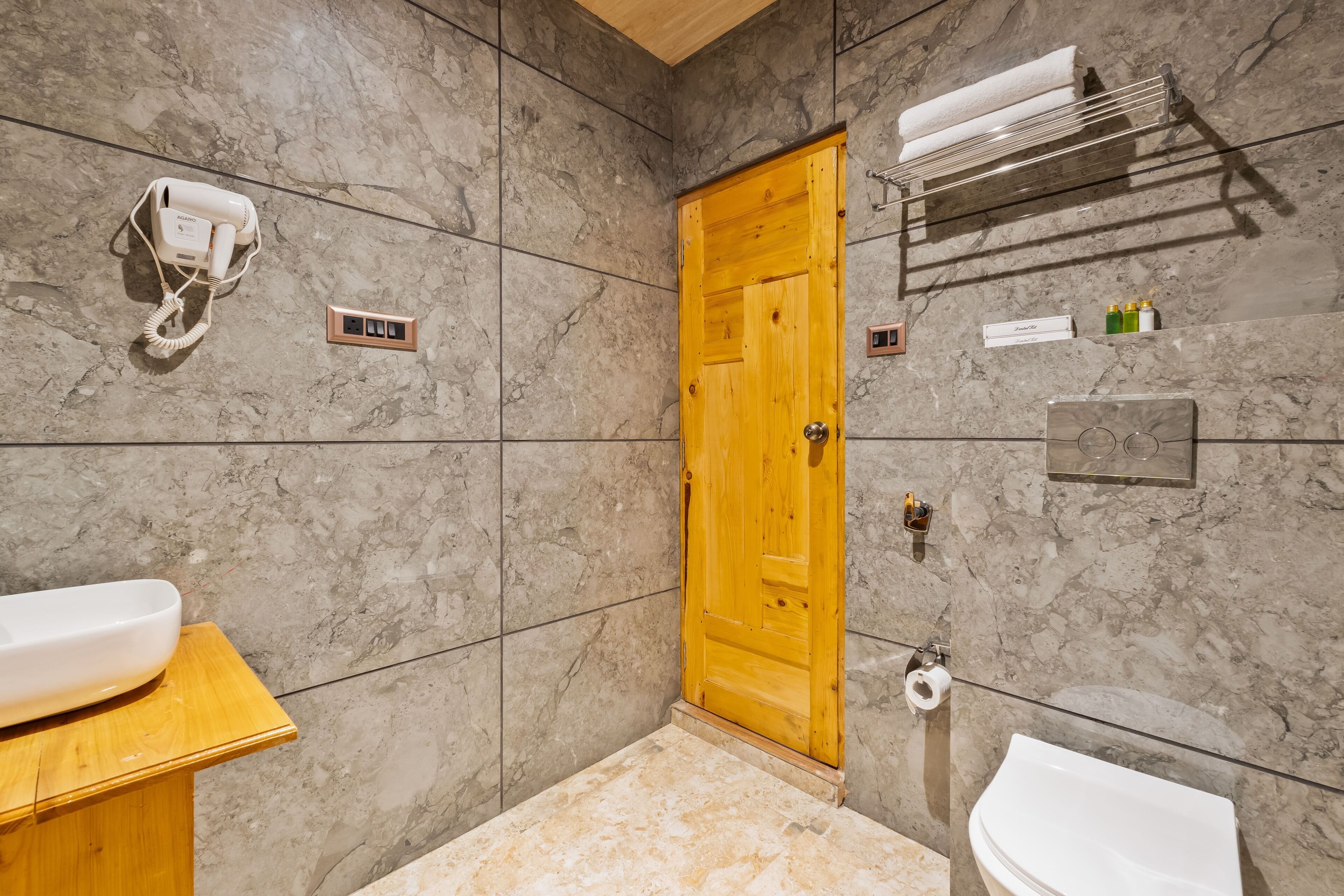 Une salle de bain avec une porte en bois, un porte-serviettes, un sèche-cheveux, un lavabo et des toilettes.