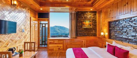 A wooden cabin interior with a bed, a television, a stone wall, and a view of mountains.