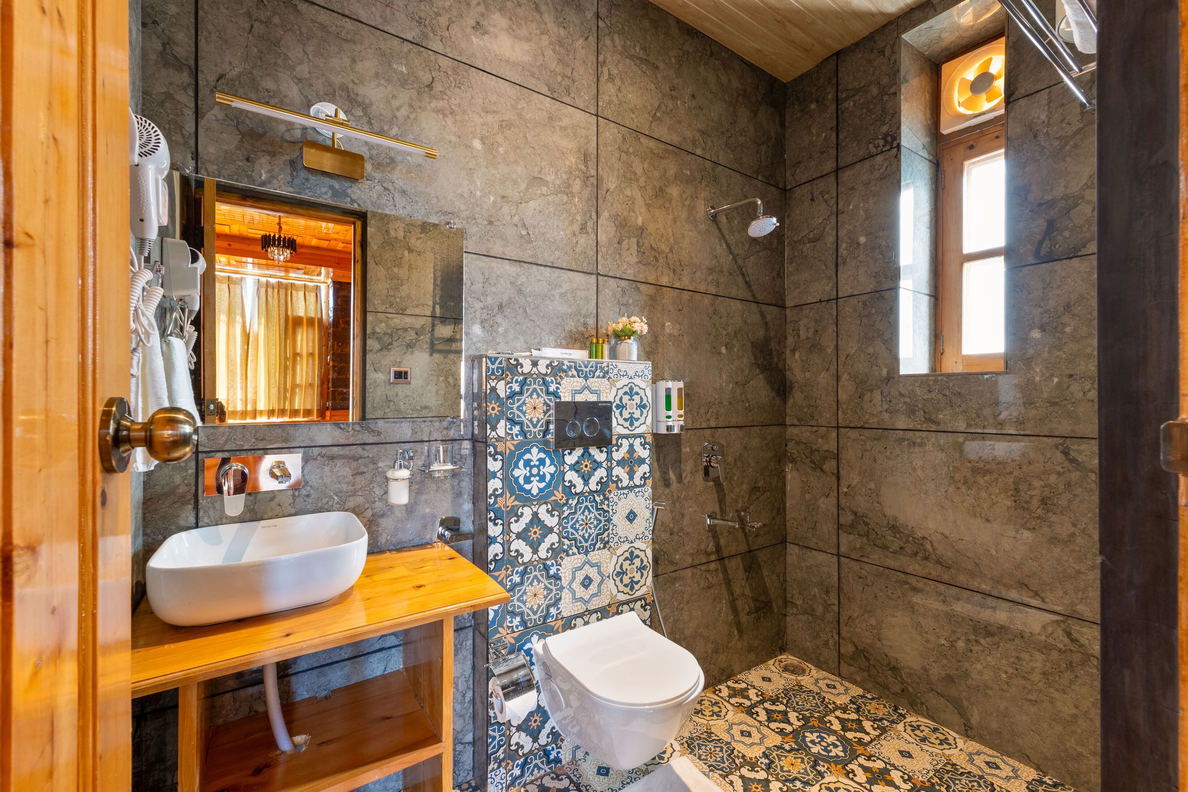 A bathroom with a wooden vanity, a white sink, a toilet, and a shower area.