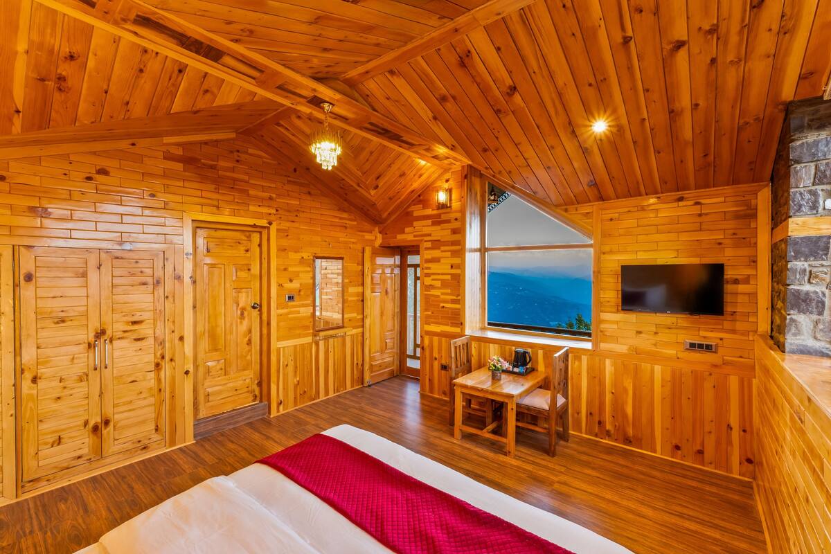 Una habitación tipo cabaña de madera con paredes de madera, una cama grande, un televisor y una chimenea de piedra.