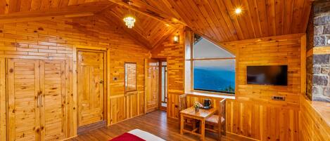 A log cabin room with wooden walls, a large bed, a TV, and a stone fireplace.