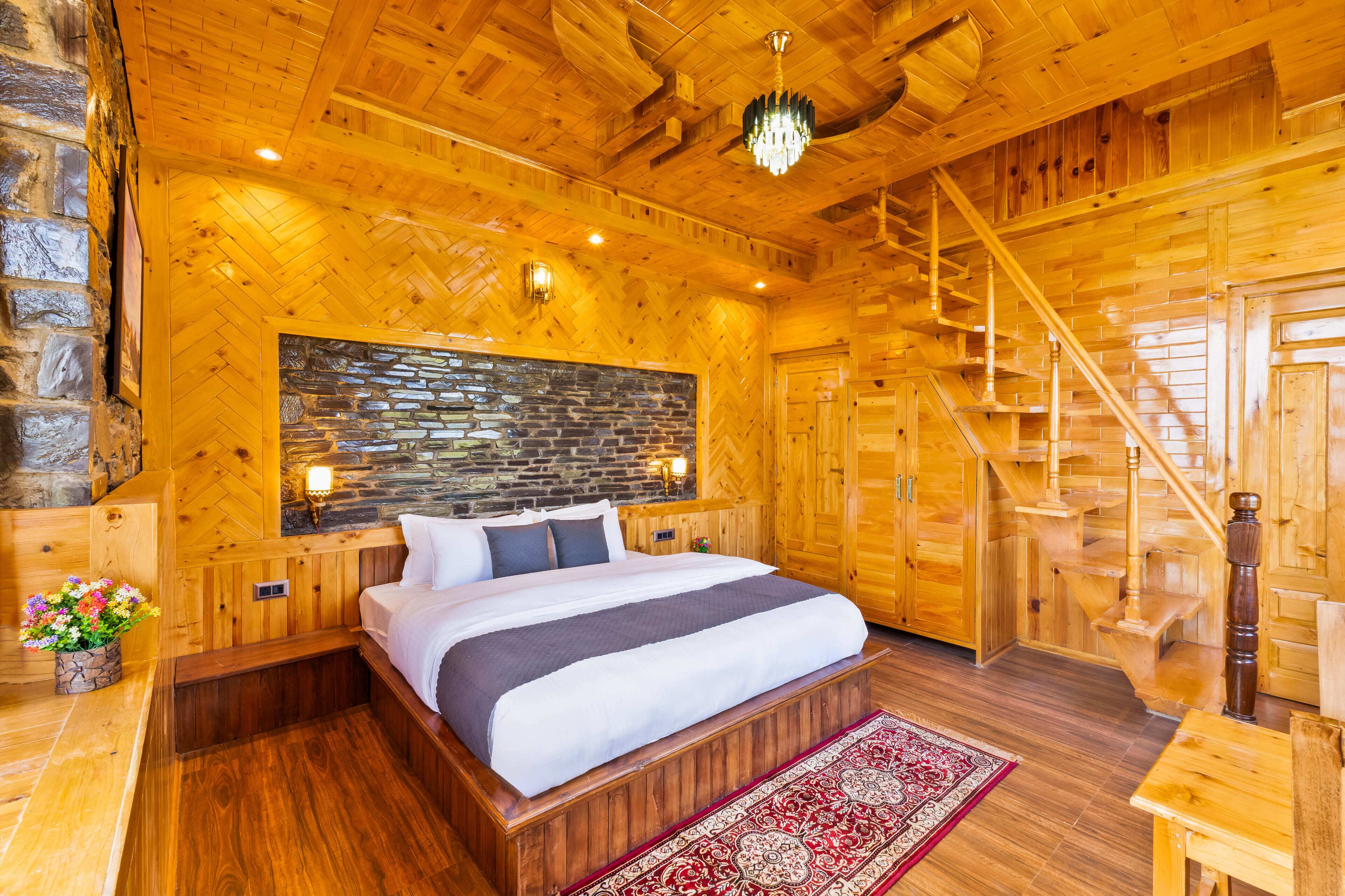 A wooden cabin-style bedroom with a bed, a stone accent wall, a chandelier, and a staircase.