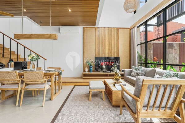 A modern living room with a wooden dining table, chairs, a sofa, and a TV. - Solana Villa by Kozystay - Canggu (Canggu)