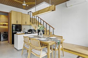 A modern kitchen with wooden cabinets, a dining area with a wooden table and chairs, and a staircase with a wooden railing. - Solana Villa by Kozystay - Canggu (Canggu)