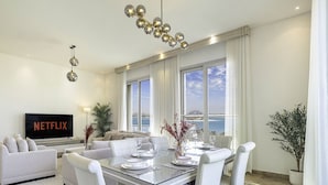 A modern living room with a dining area, a flat-screen TV, and a view of the city. - LUX Dream Palm Atlantis Sea View Suite (Dubai)