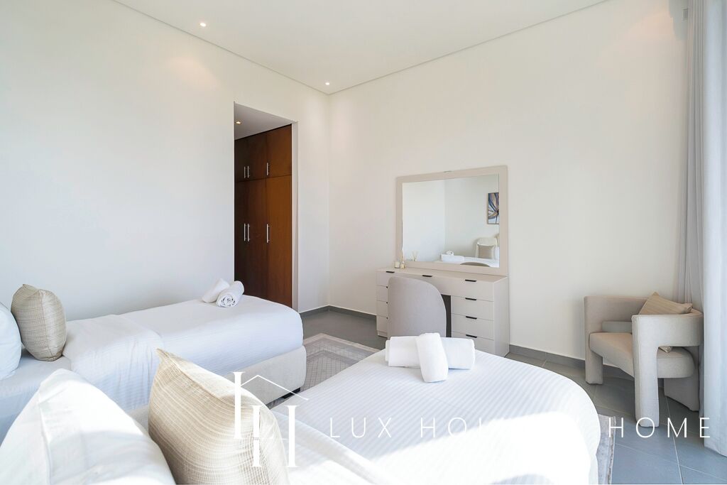 A modern hotel room with two beds, a vanity with a mirror, and a seating area.