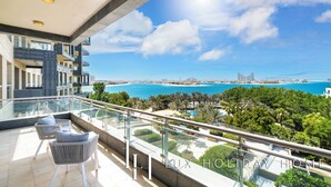 A balcony with a glass railing overlooking a beach and ocean. - LUX Dream Palm Atlantis Sea View Suite (Dubai)