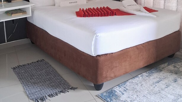 A neatly arranged bedroom with a large bed, a bedside table, a nightstand, and a window with curtains. - Shalakwe Hills-Inn Guesthouse (Kasane)