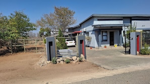 A modern building with a gated entrance, a paved driveway, and a parked car. - Shalakwe Hills-Inn Guesthouse (Kasane)