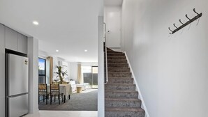 Un intérieur moderne avec un escalier menant à un deuxième étage, un coin repas avec une table et des chaises, et un espace cuisine équipé d’un réfrigérateur.