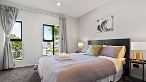 Une chambre d’hôtel moderne avec un grand lit, des rideaux gris, une vue sur l’extérieur et un tableau au mur.