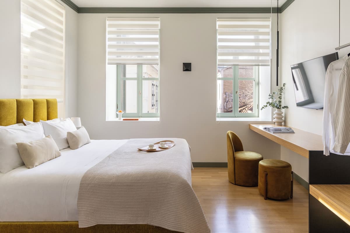 Una habitación de hotel moderna con una cama grande, dos ventanas con persianas, un escritorio con una silla y un televisor.