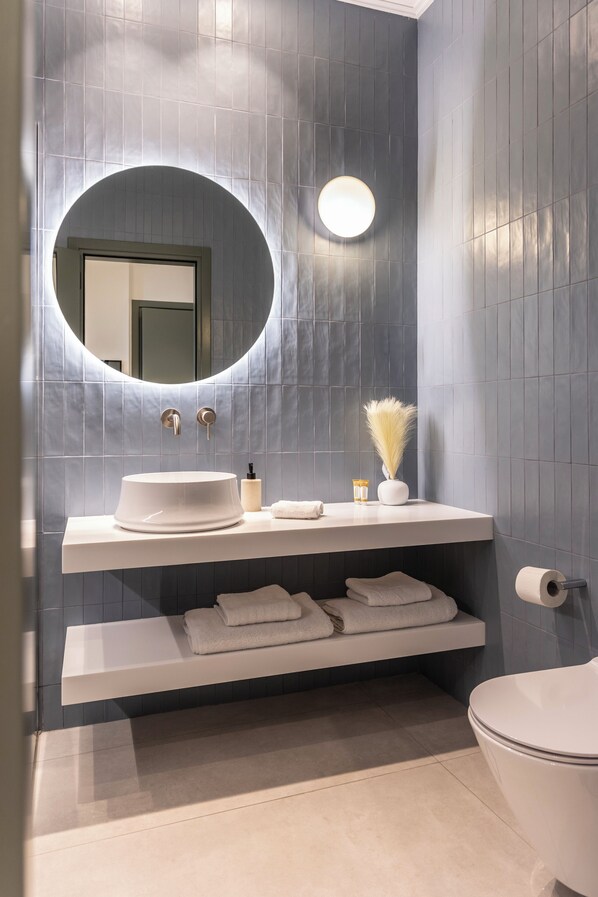 A modern bathroom with a round mirror, white sink, and a toilet. - Whisper Athens Suites. (Athens)