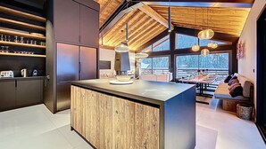 Una cocina moderna con una isla de madera, armarios oscuros y vistas al exterior a través de amplios ventanales.