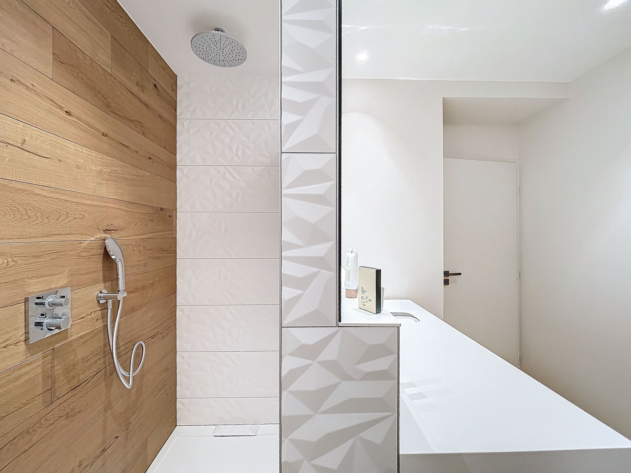 A modern bathroom with a wooden wall, a shower, and a white vanity with a geometric tile backsplash.