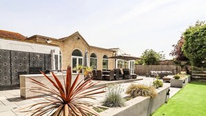 Un espace patio avec des sièges d’extérieur, un mur décoratif et une pelouse bien entretenue.