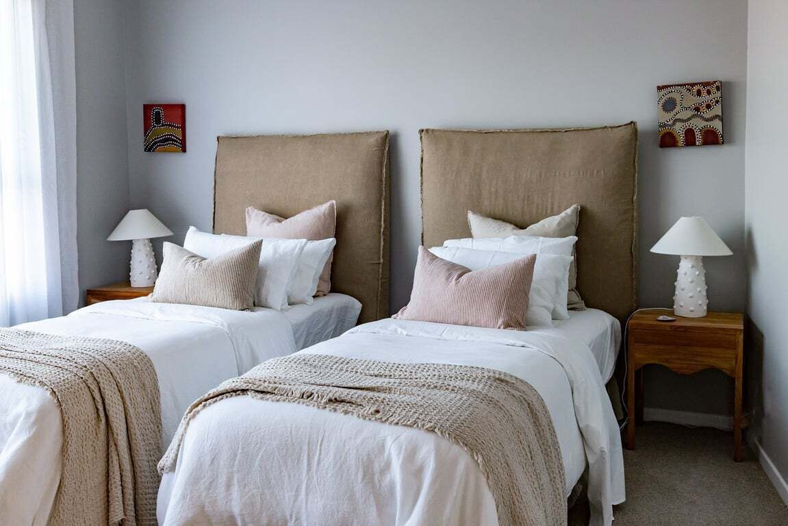 A double room with two beds, each with a headboard, white bedding, and a lamp on a bedside table.