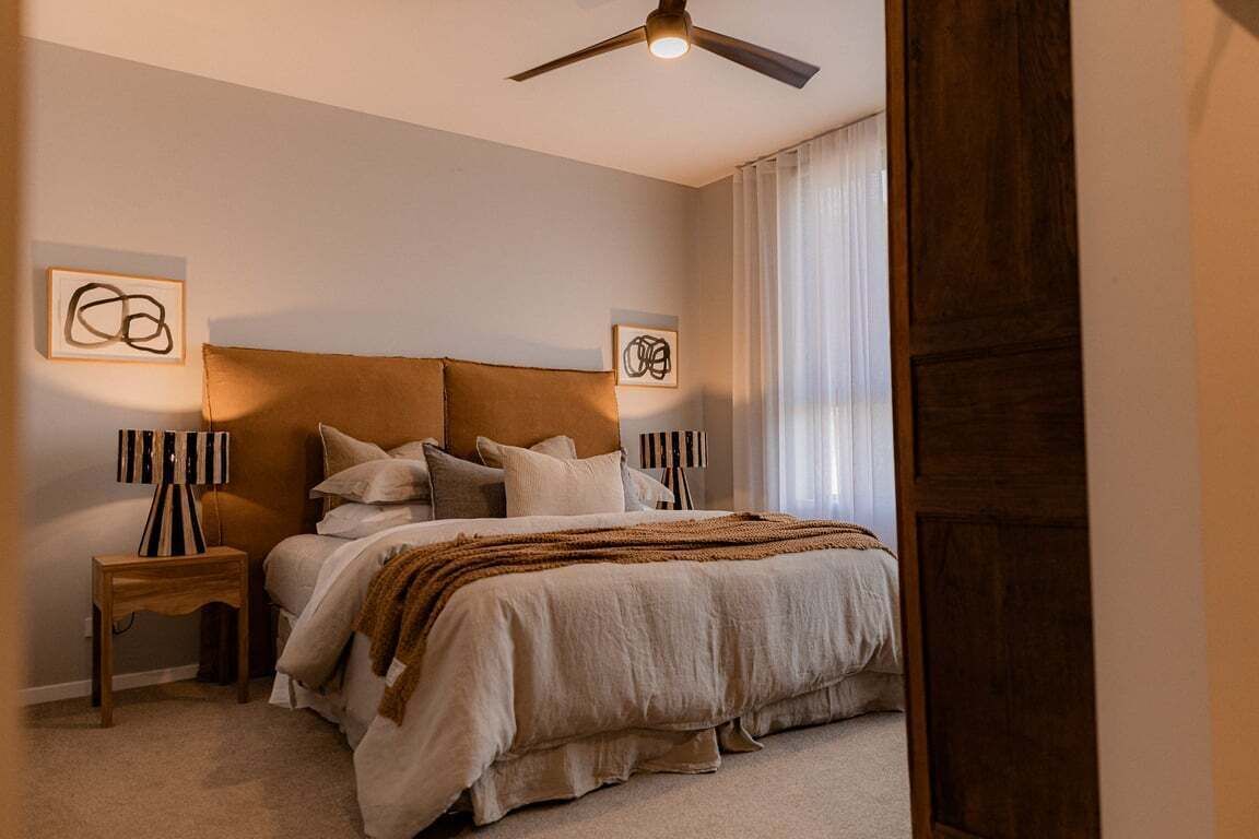 A bedroom with a large bed, two bedside tables, a ceiling fan, and artwork on the walls.
