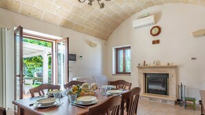 Uma área de jantar com mesa de madeira posta para quatro pessoas, lareira e vista para o exterior.