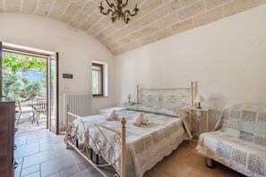 A bedroom with a bed, a chair, a table, and a view of the outside. - Tenuta Guarini Trulli On Selva Di Fasano (Fasano)