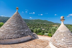 Two stone-roofed structures with a view of a green landscape and hills in the background. - Tenuta Guarini Trulli On Selva Di Fasano (Fasano)