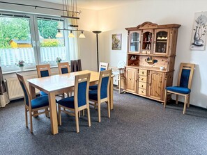 Spisestue med et træbord og stole, et skab med glaslåger og et vindue med gardiner.