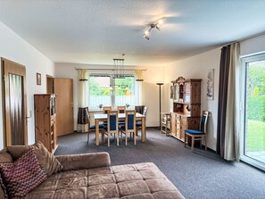 Ein Zimmer mit einer Couch, einem Esstisch, Stühlen, einem Schrank und einem großen Fenster.