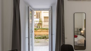 A hotel room with a sliding glass door leading to a courtyard, a bed, a chair, and a mirror on the wall. - Welcome Rome by Interhome (Rome: Historical City Center)