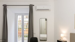 A hotel room with a bed, a chair, a nightstand with a lamp, a large mirror, and an air conditioning unit. - Welcome Rome by Interhome (Rome: Historical City Center)