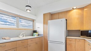 Une cuisine avec des meubles en bois, un réfrigérateur blanc, un évier avec un robinet et une fenêtre donnant sur le ciel.