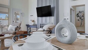 Un salon moderne avec un téléviseur à écran plat fixé au mur, un grand vase décoratif et un coin repas avec de la vaisselle blanche et des couverts.