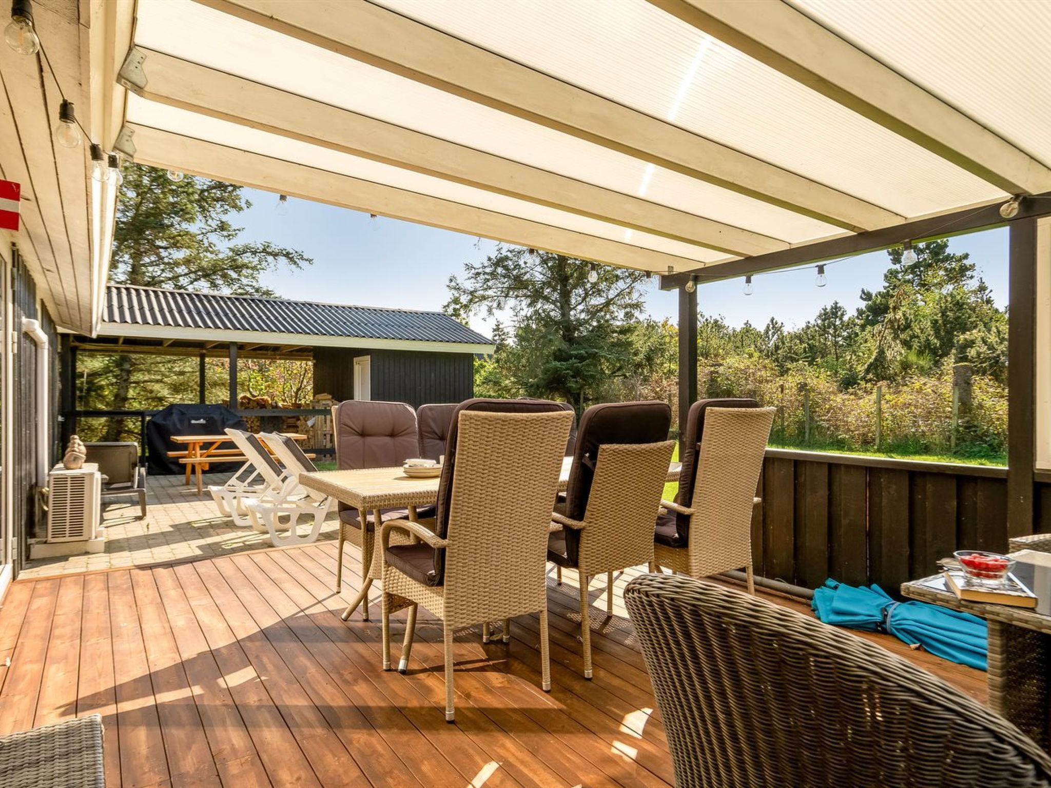 An outdoor patio with wicker furniture, a barbecue grill, and a view of the surrounding trees.