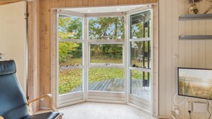 Ein Eckzimmer mit Erkerfenster, einem blauen Sessel und einem Fernseher an der Wand.