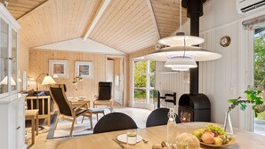 Ein gemütliches Blockhaus mit Essbereich, Holzwänden, einem großen Fenster und einem Kamin.