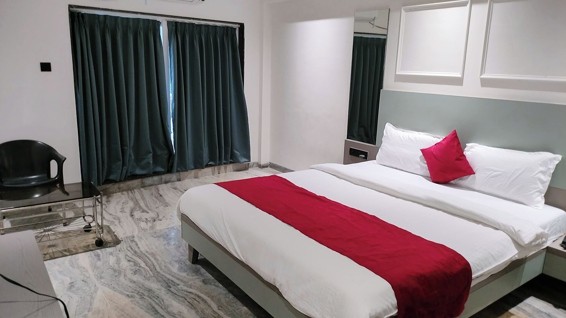 Ein Hotelzimmer mit Bett, Stuhl, Nachttisch und einem Fenster mit Vorhängen.