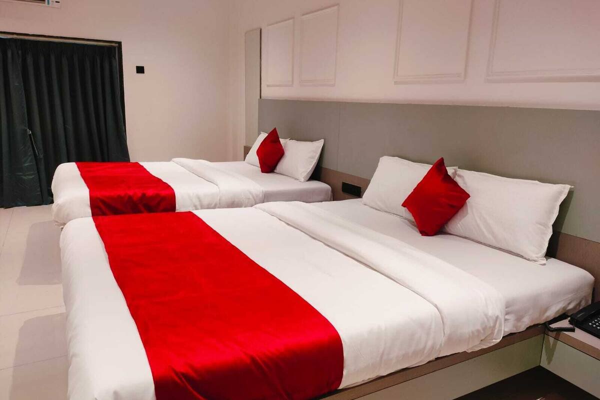 Ein Hotelzimmer mit zwei Betten, jeweils mit weißer Bettwäsche und roten Akzenten, einem Nachttisch mit Telefon und einem Fenster mit Vorhängen.