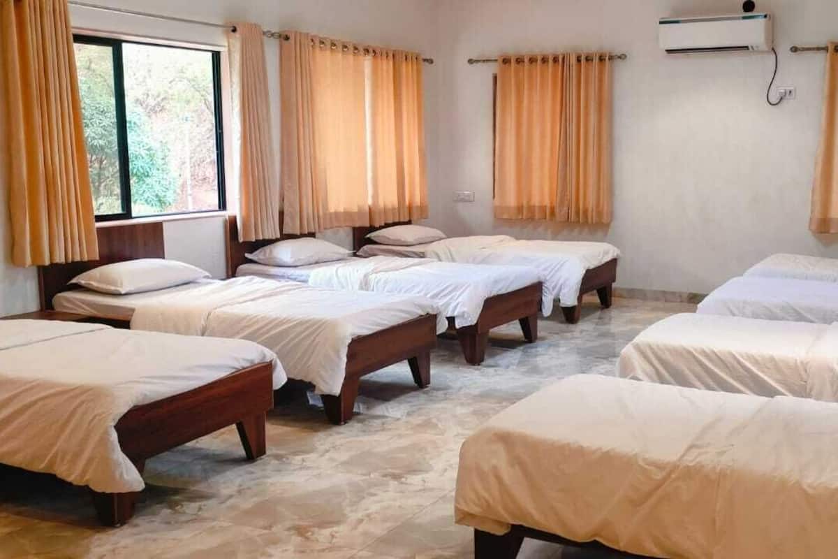 Ein Hotelzimmer mit mehreren Betten, beigen Vorhängen, einem Fenster und einer Klimaanlage.