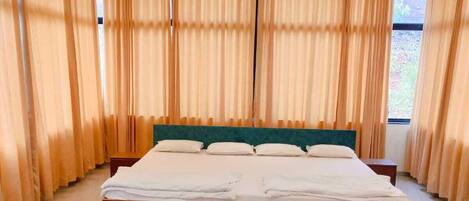 Un dormitorio con una cama grande, una araña, cortinas y una mesa de vidrio.